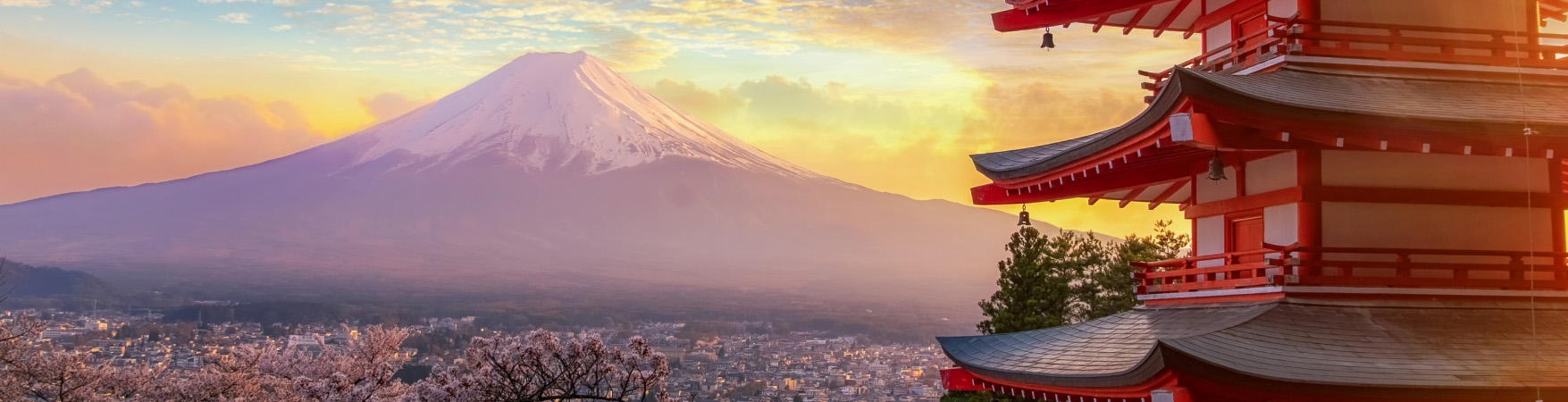 Paisagem do Japão com o Monte Fuji ao fundo, parcialmente coberto de neve. Em primeiro plano, há uma pagoda tradicional japonesa de cinco andares, pintada em vermelho e branco. Ao redor, cerejeiras em plena floração exibem flores rosa claro. O céu ao entardecer está colorido com tons de laranja e amarelo, criando uma atmosfera serena e encantadora. A imagem combina elementos naturais e culturais, representando a beleza típica do Japão.